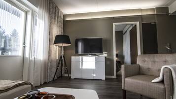 A modern living room with a sofa, a TV on a white cabinet, a lamp, and a window with curtains.