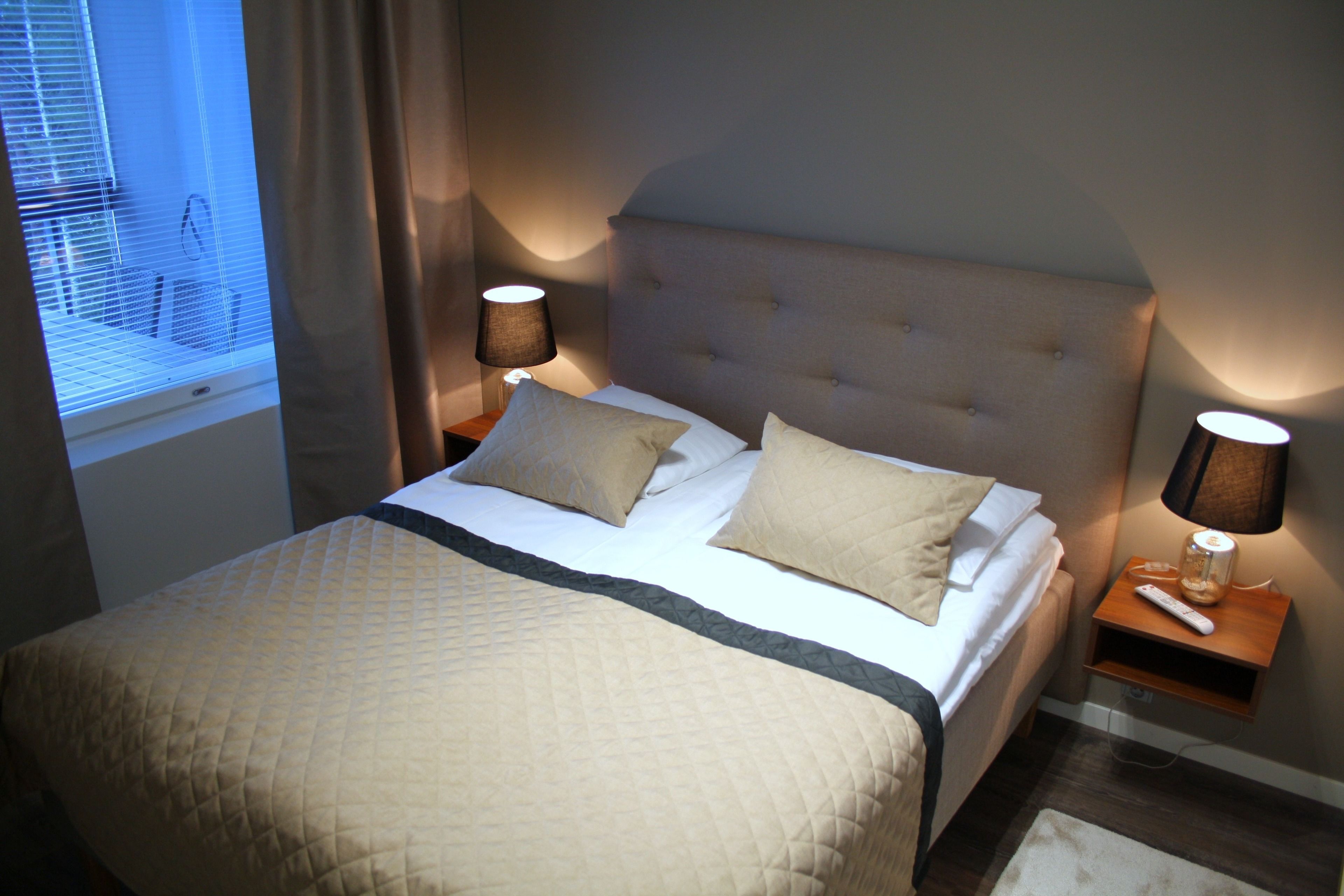 A neatly made bed with a quilted cover, two bedside lamps, and a nightstand with a remote control.