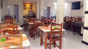 A dining area with multiple wooden tables and chairs, a tiled floor, and a television mounted on the wall. - Pousada Panoramica (Aracaju)