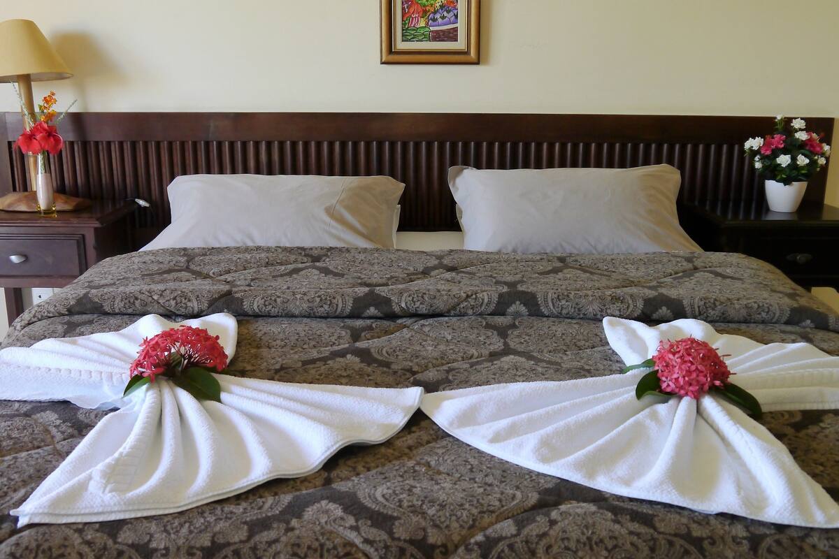 A neatly made bed with patterned bedding, two pillows, and towels arranged in a decorative manner with flowers.