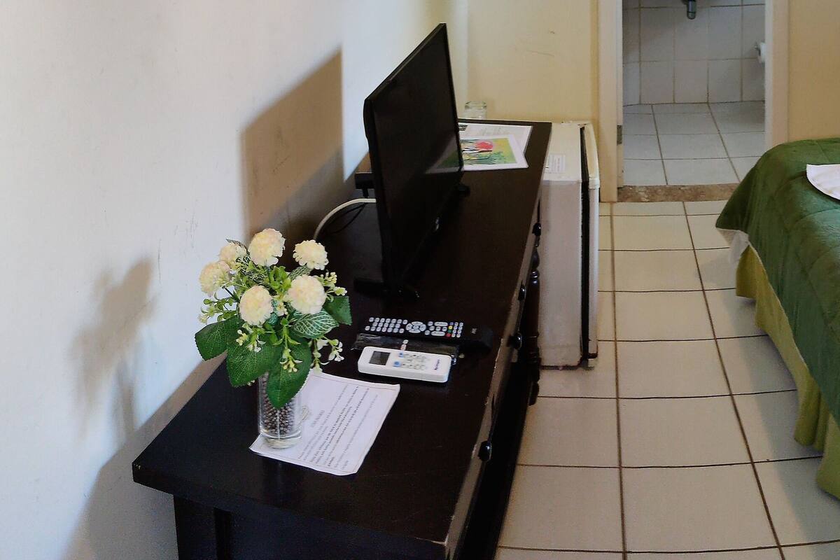 A hotel room with a green bed, white pillows, and a bouquet of flowers on the nightstand.