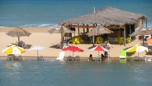 A beachside resort with thatched-roof huts, sun umbrellas, and lounge chairs. - Grimms Pousada de Contos (Entre Rios)