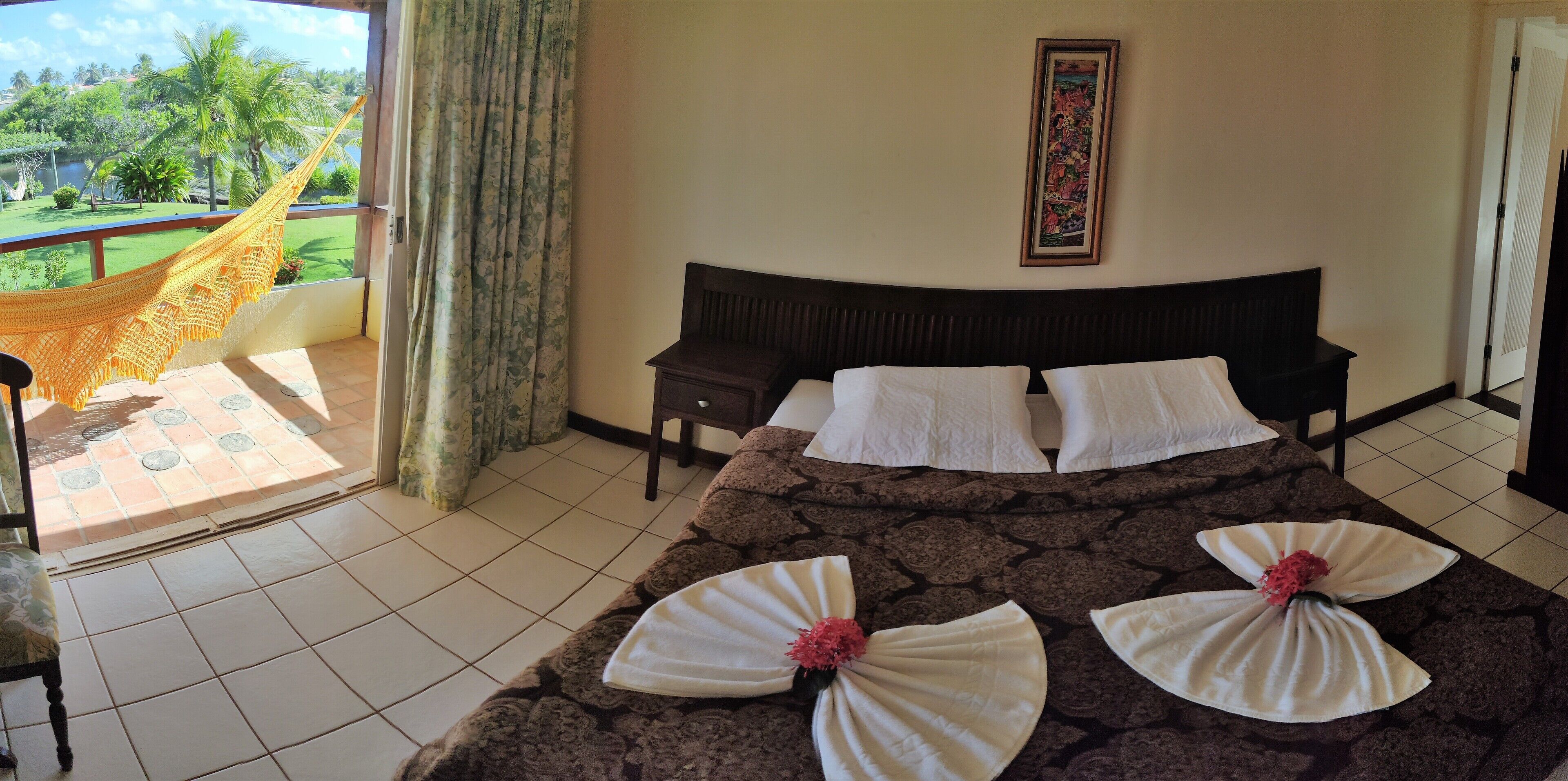 Habitación de hotel con cama, mesita de noche, silla, hamaca y vista a un jardín.