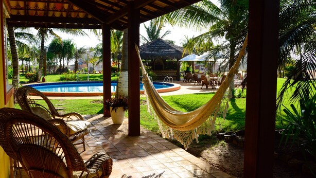 A covered outdoor area with a pool, hammocks, and wicker chairs. - Grimms Pousada de Contos (Entre Rios)