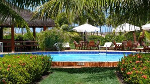 A pool area with lounge chairs and umbrellas, surrounded by lush greenery and a thatched-roof structure. - Grimms Pousada de Contos (Entre Rios)
