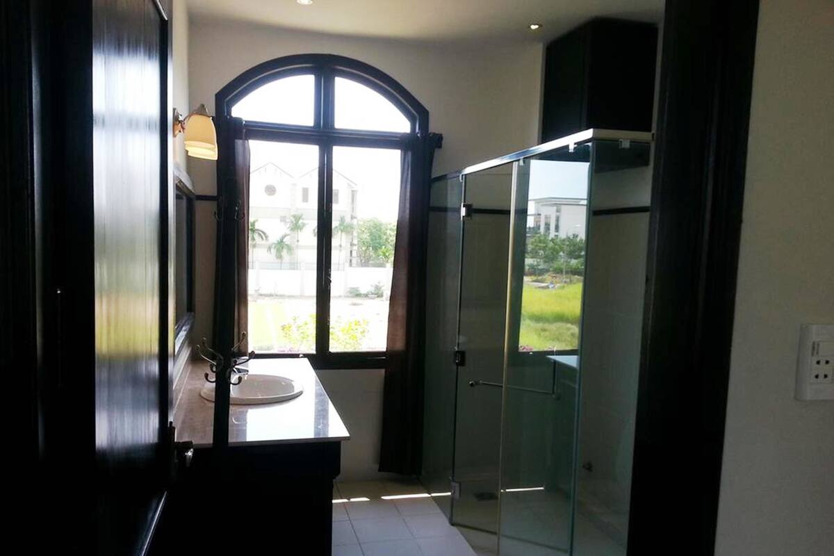 A bathroom with a large arched window, a glass shower enclosure, and a sink with a mirror.