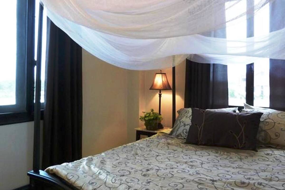 A bedroom with a bed, a nightstand, a lamp, and a window with curtains.