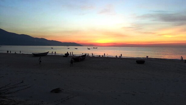 Una platja amb vaixells i persones al capvespre.