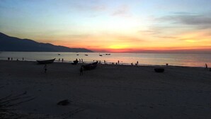 A beach with boats and people during sunset.