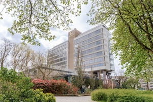 Un moderno edificio de hotel con varios pisos, fachada de vidrio y un jardín bien cuidado con diversas plantas y arbustos.