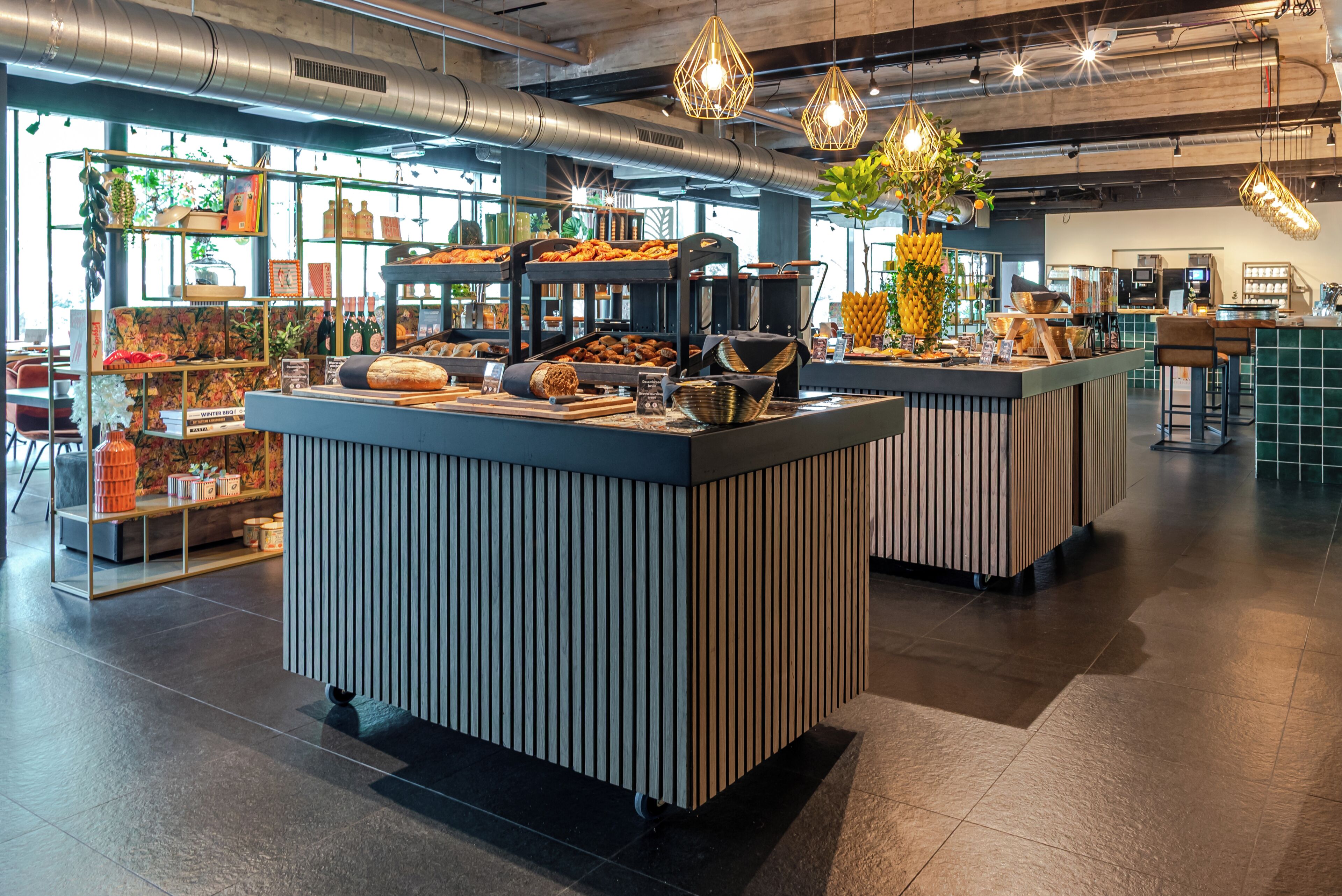A modern cafe with a central counter, shelves with baked goods, and hanging lights.