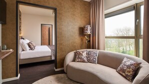 A modern hotel room with a curved sofa, a bed with white bedding, a large mirror, and a window with curtains. - Hotel Wander (Wageningen)
