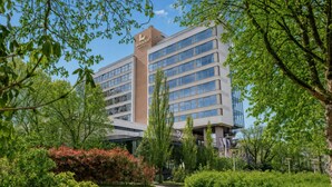 A modern hotel building with multiple floors, a prominent sign, and surrounded by lush greenery. - Hotel Wander (Wageningen)