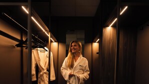 A person in a white robe standing in a hallway with wooden flooring and mirrored walls. - Hotel Wander (Wageningen)
