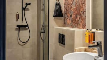 Een moderne badkamer met douche, toilet en wastafel, met tropisch bladbehang en een grote spiegel.
