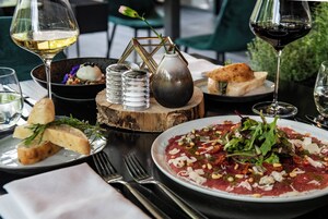 A dining table with plates of food, glasses of wine, and a vase with a flower.