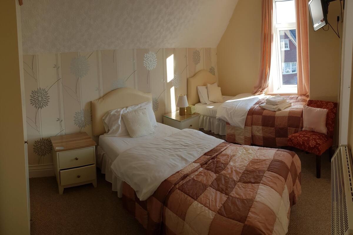 A bedroom with two beds, a nightstand, a lamp, and a window with curtains.