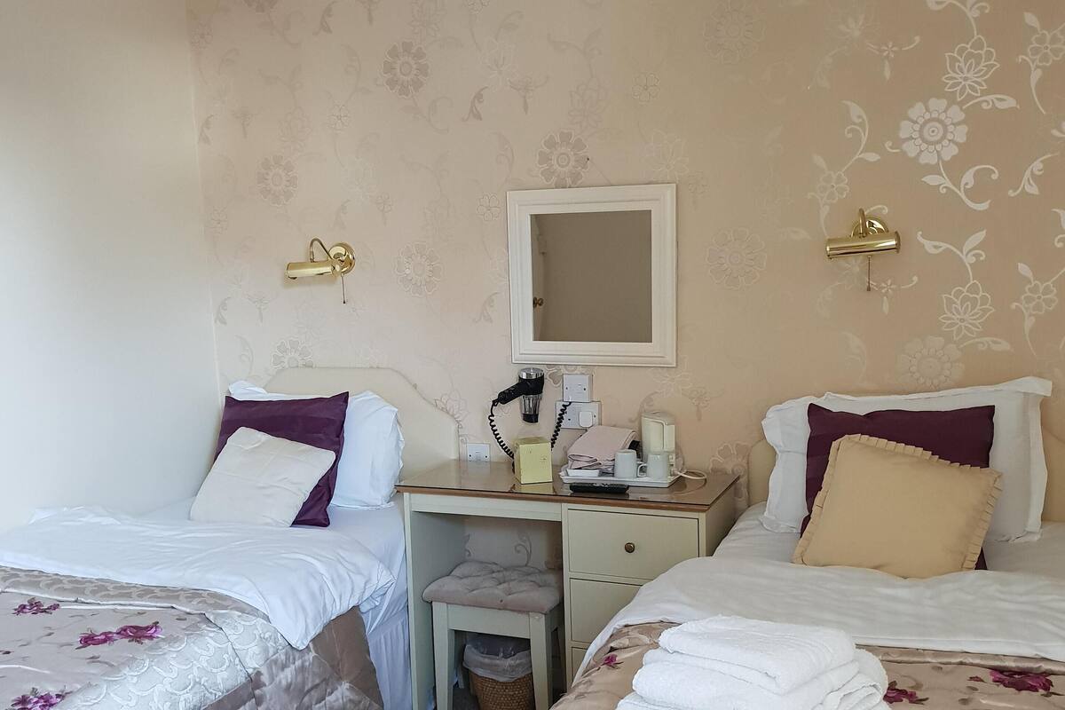 A hotel room with two beds, a desk, a chair, a mirror, and a trash bin.