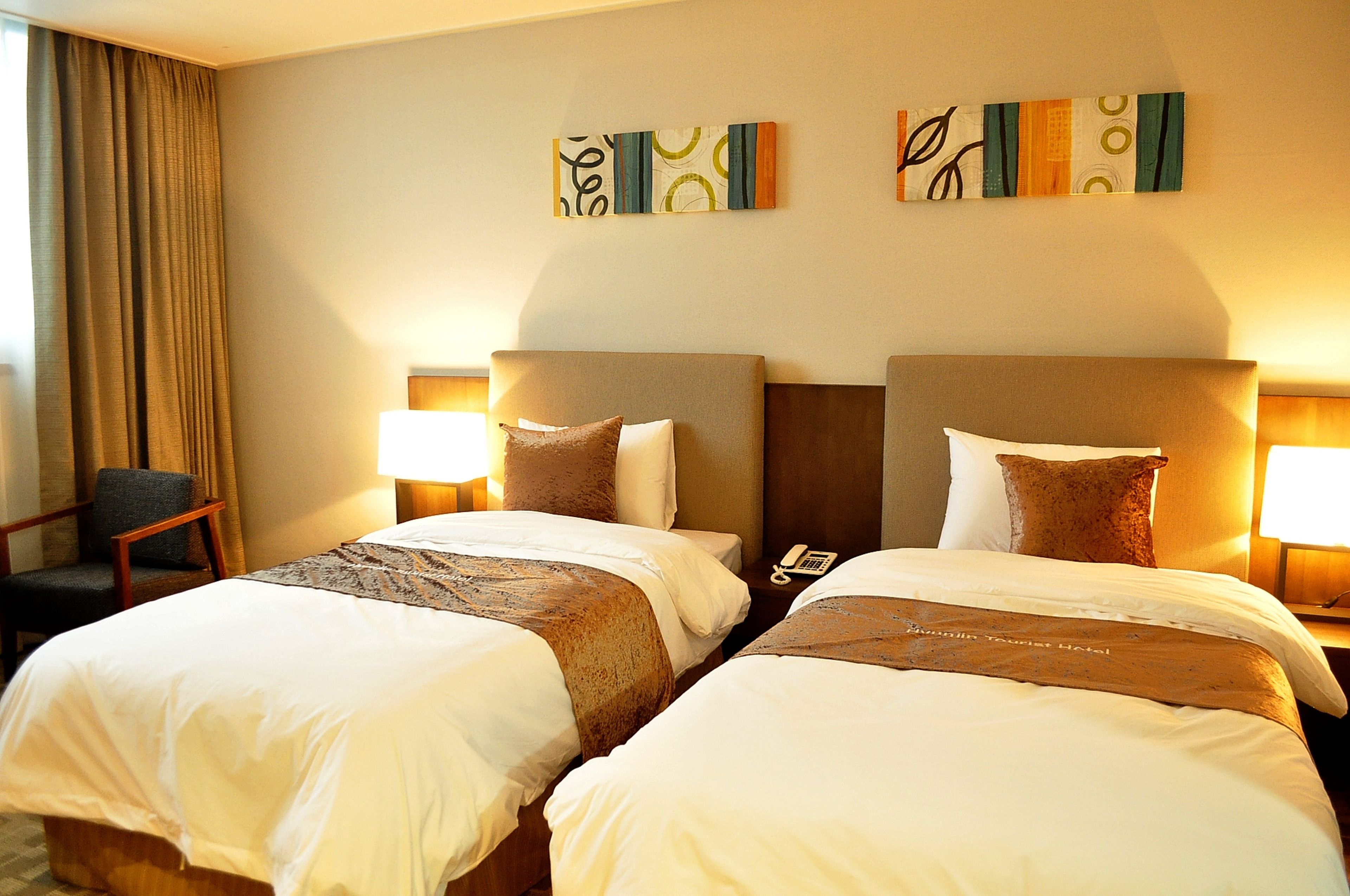 A hotel room with two beds, a chair, and artwork on the wall.