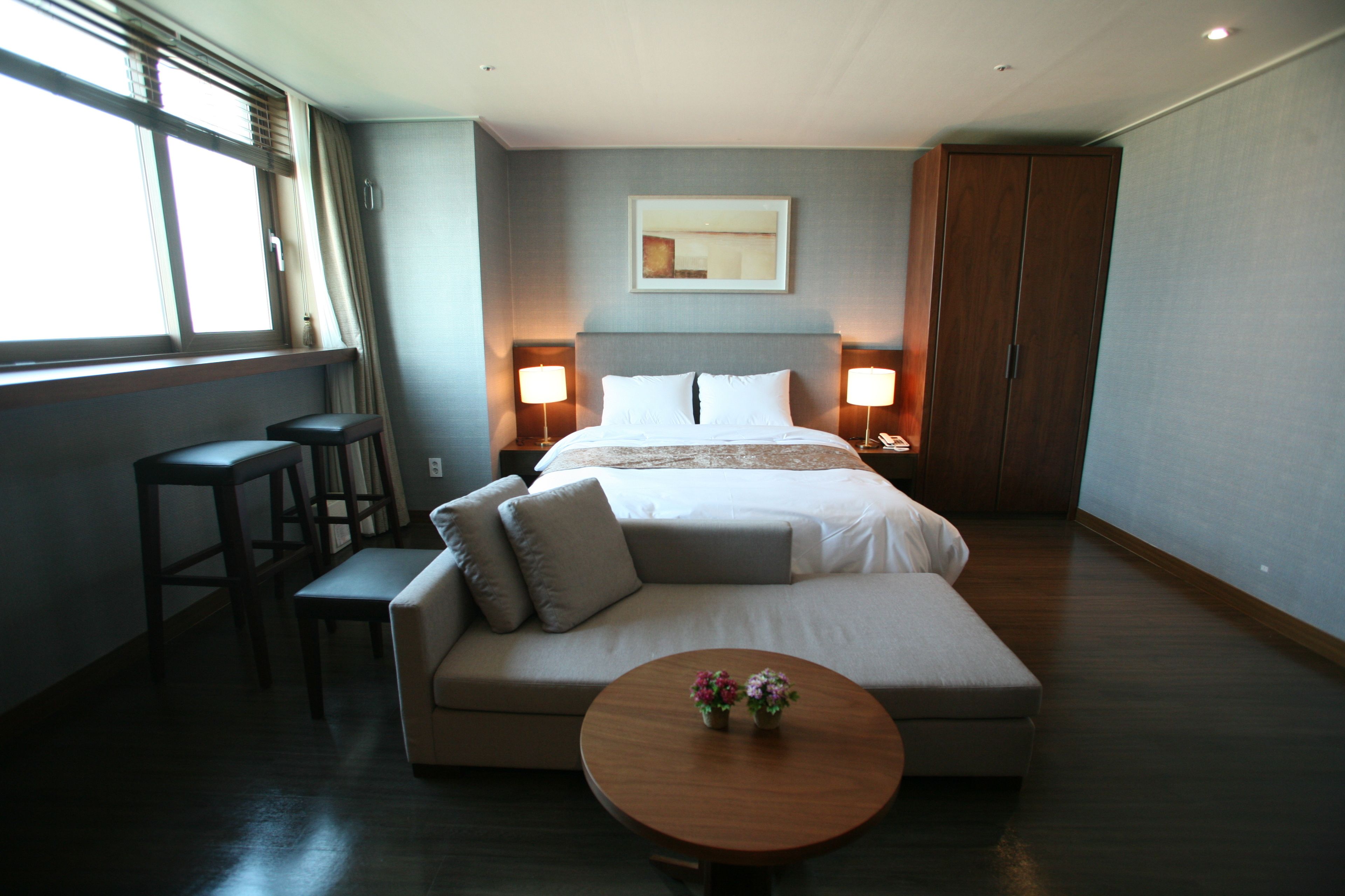 Una habitación de hotel moderna con una cama grande, un sofá, una mesita con flores, dos lámparas de noche y un armario.