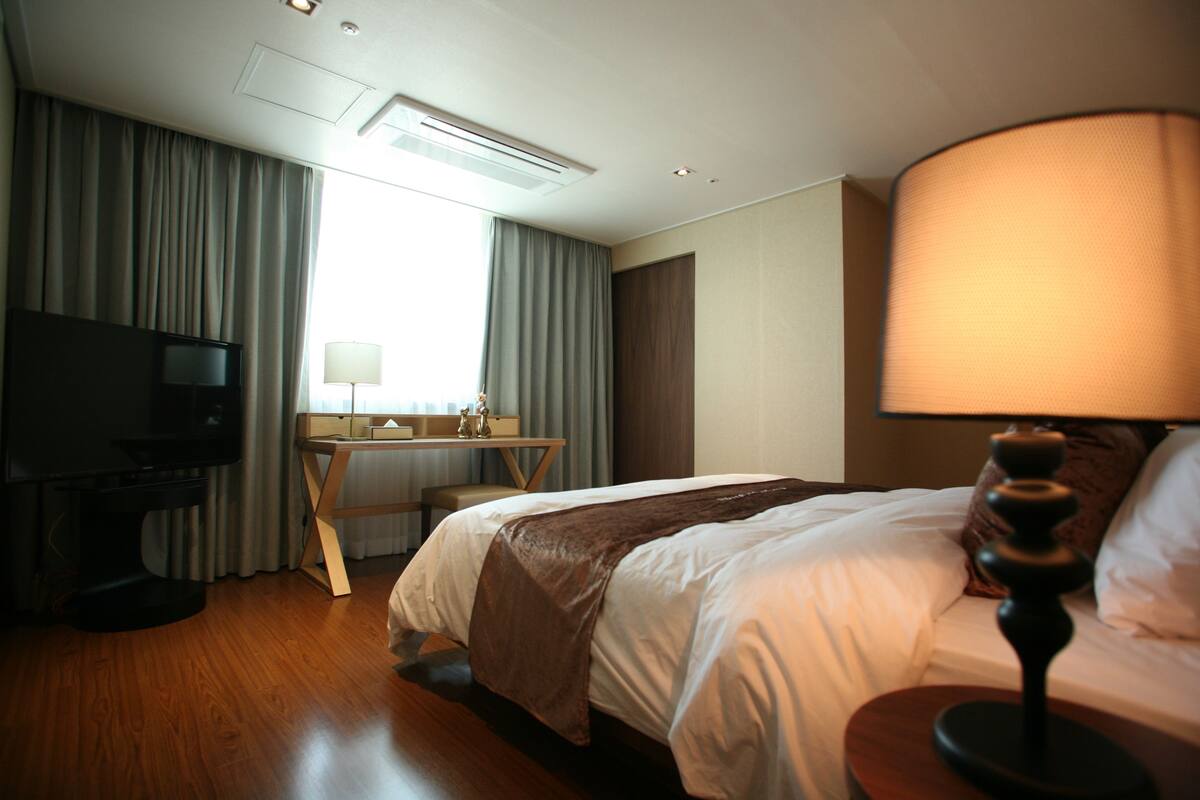 Habitación de hotel con cama, escritorio, televisión y lámpara.