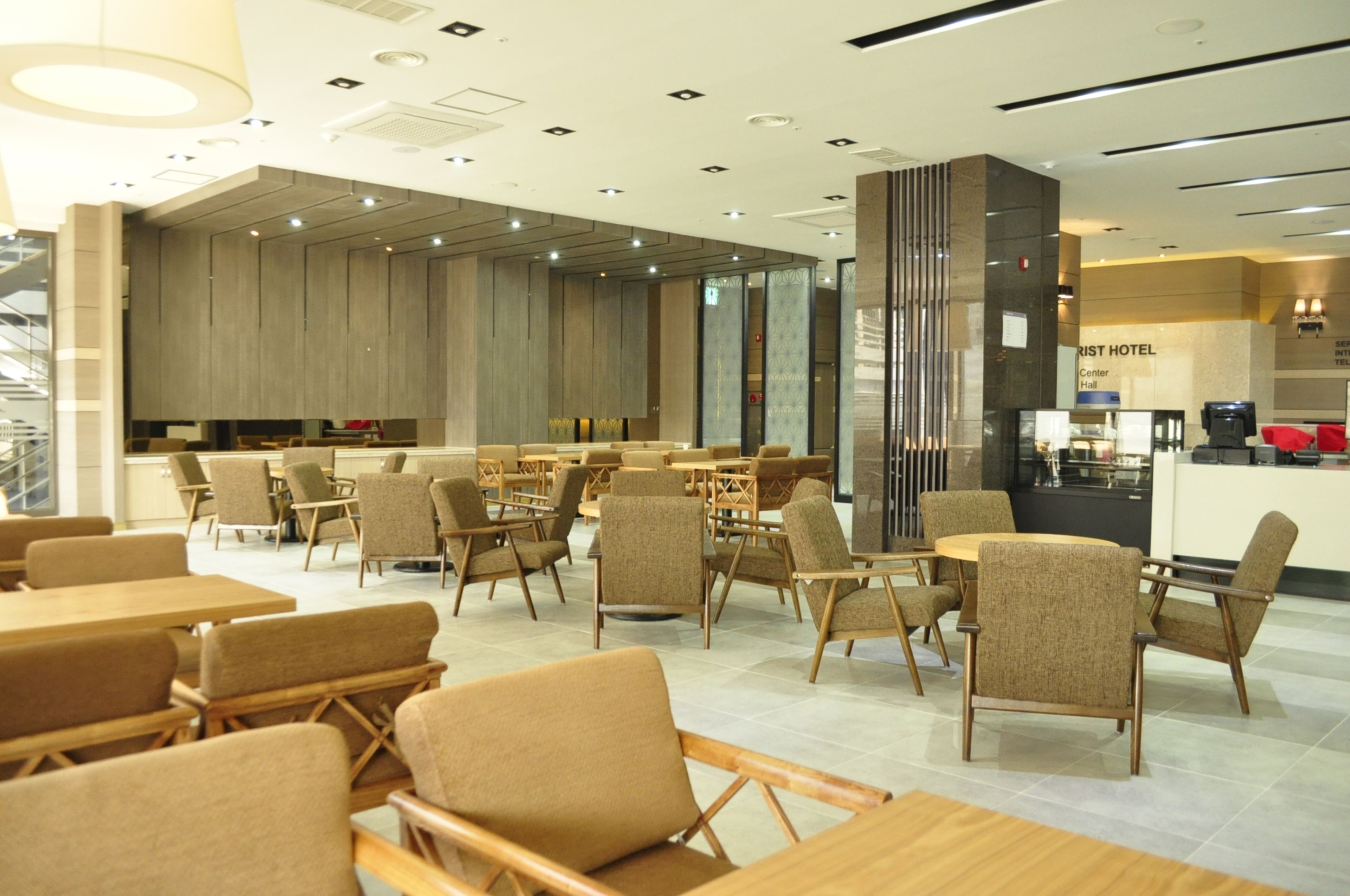 A modern hotel lobby with wooden furniture, a central bar area, and a staircase leading to an upper level.