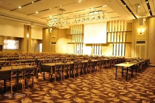 Un salón de conferencias de hotel con filas de mesas y sillas, una lámpara de araña grande y una alfombra estampada.