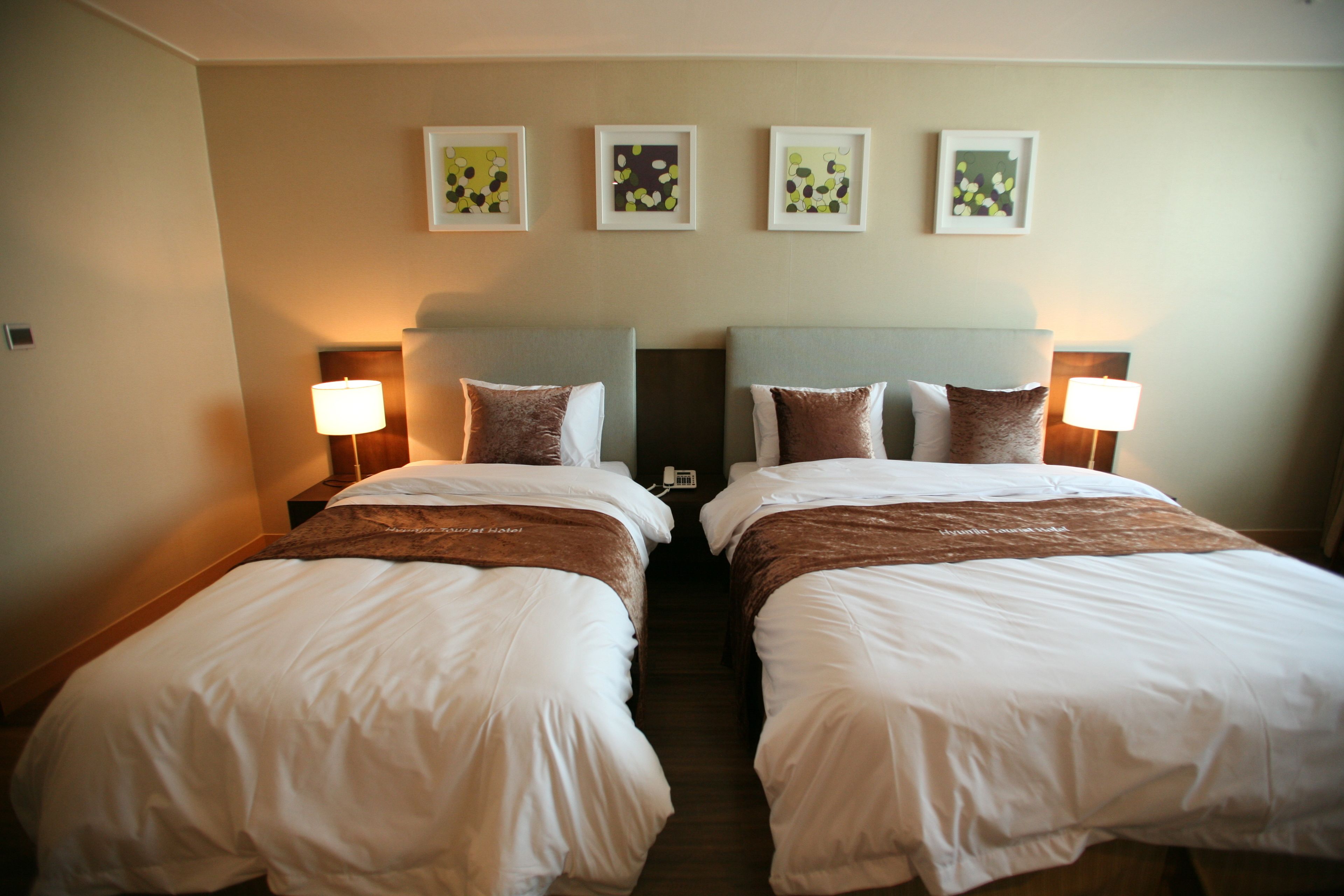 A hotel room with two beds, each with white bedding and brown headboards. There are framed pictures on the wall above the beds.