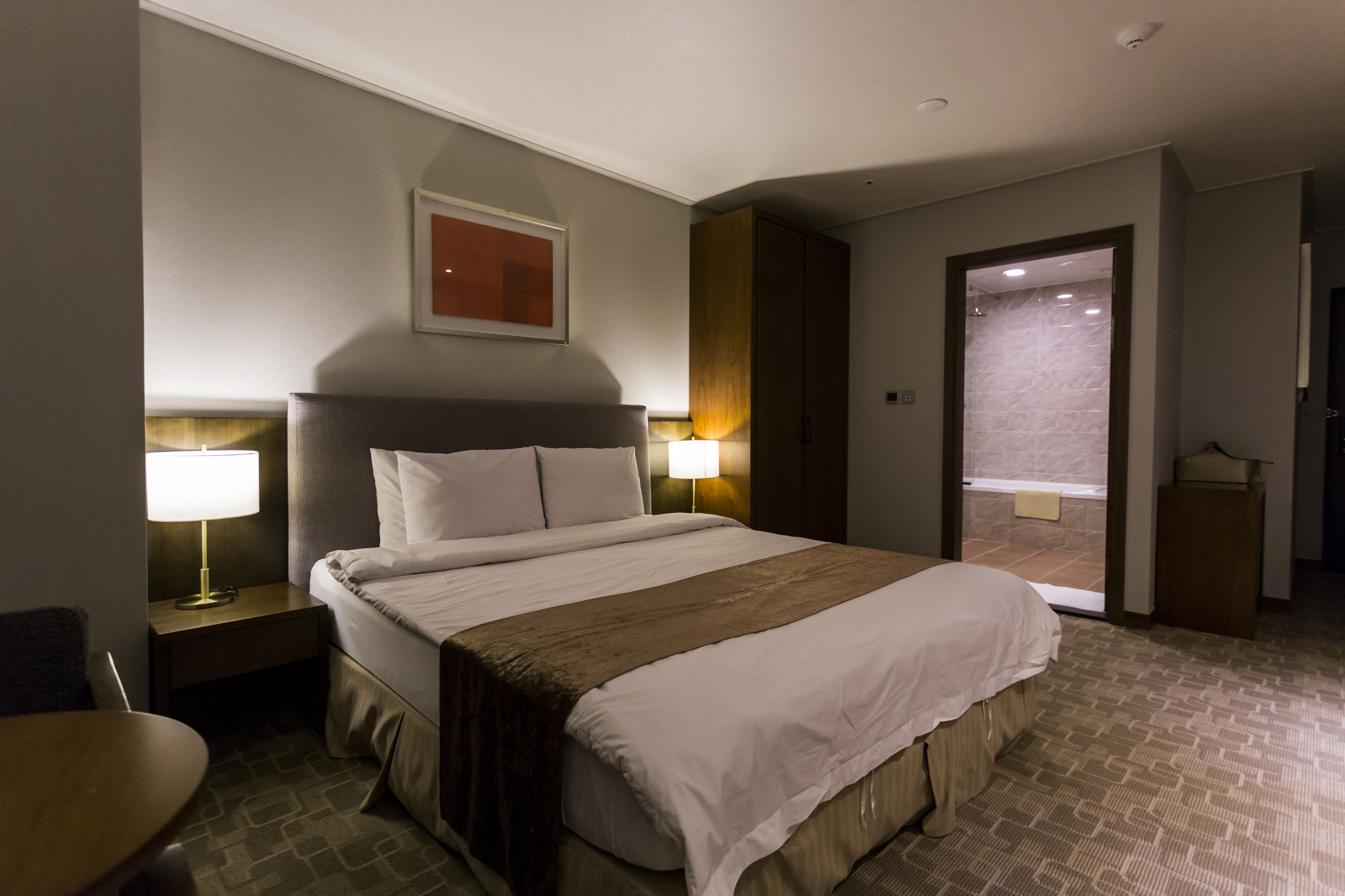 Habitación de hotel con una cama grande, lámparas de noche, una mesita y una puerta que da a un balcón.