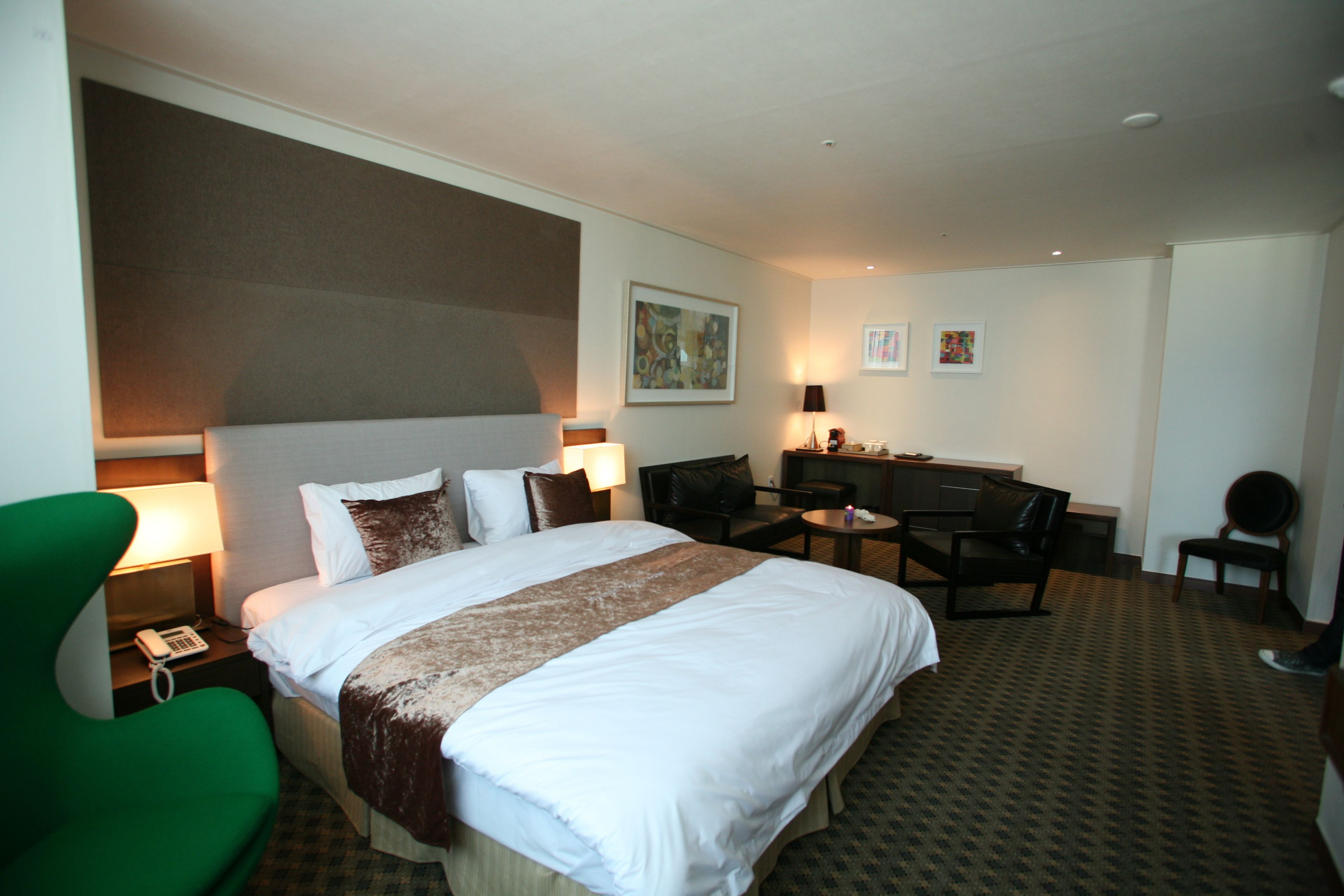 Habitación de hotel con una cama grande, un escritorio, dos sillas, una lámpara y un cuadro en la pared.