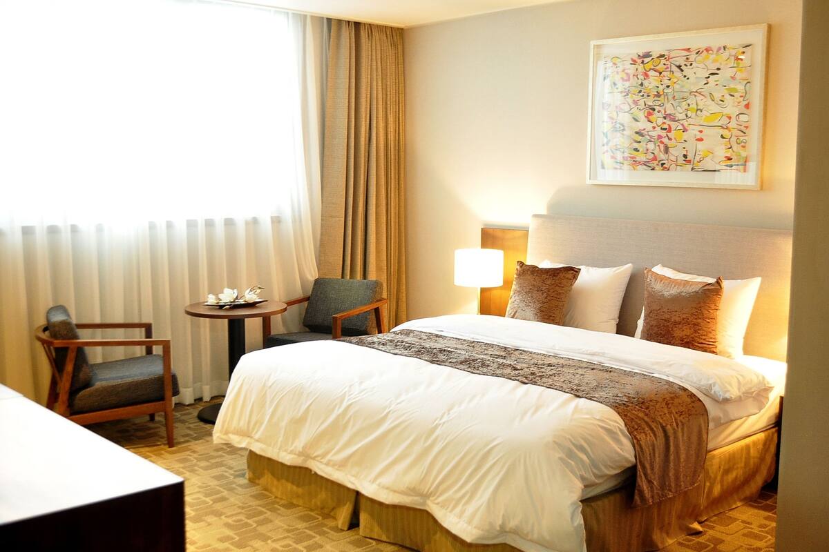 Habitación de hotel con una cama grande, una mesita con una silla, una lámpara y un cuadro en la pared.