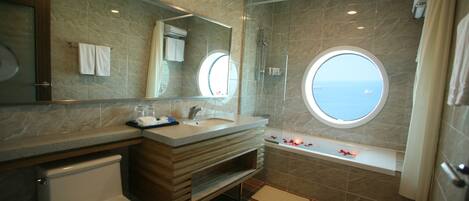 A modern bathroom with a marble vanity, a toilet, a bathtub with a view, and a glass-enclosed shower.
