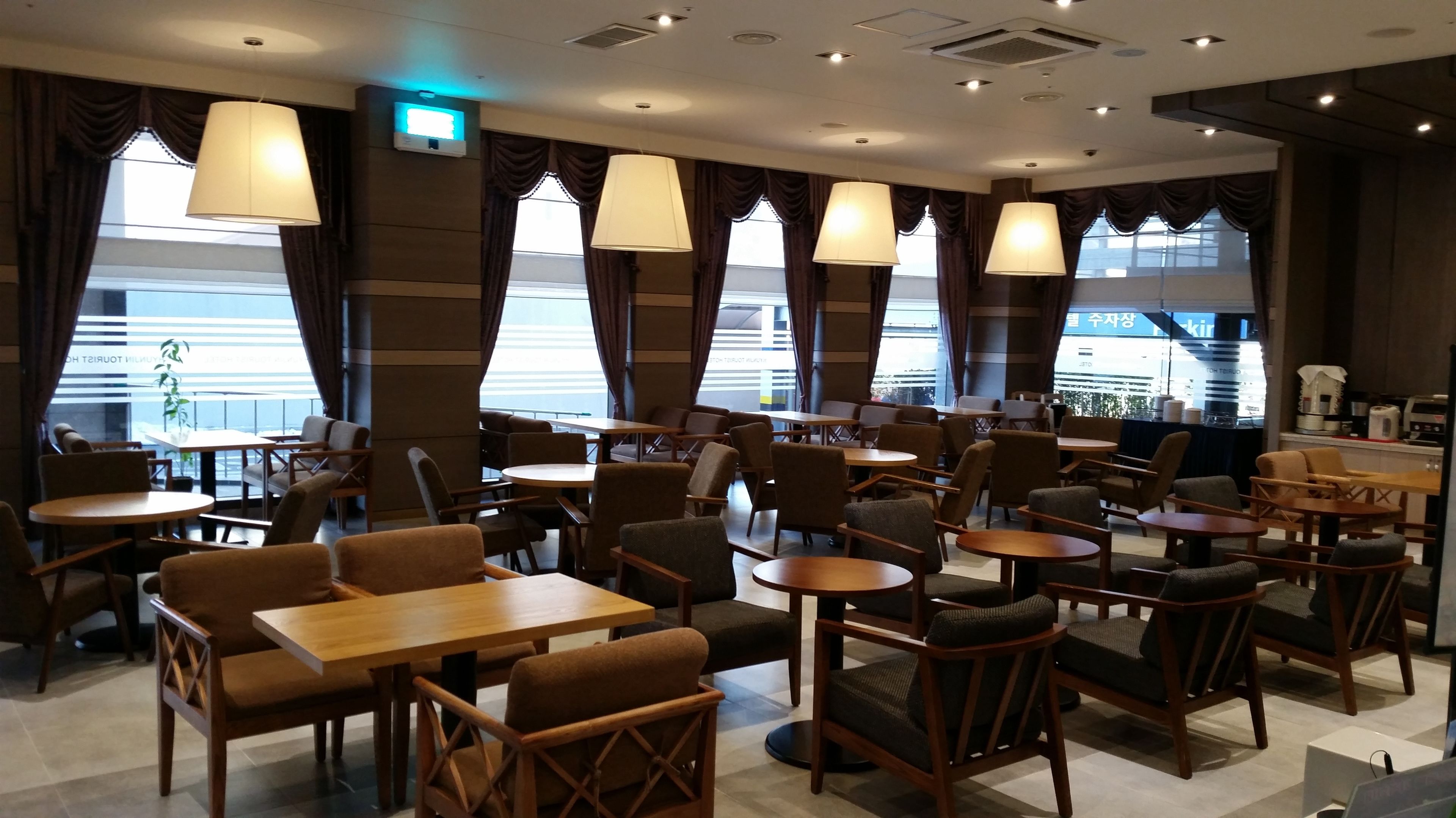 A modern restaurant with multiple seating areas, including tables and chairs, and large windows with curtains.