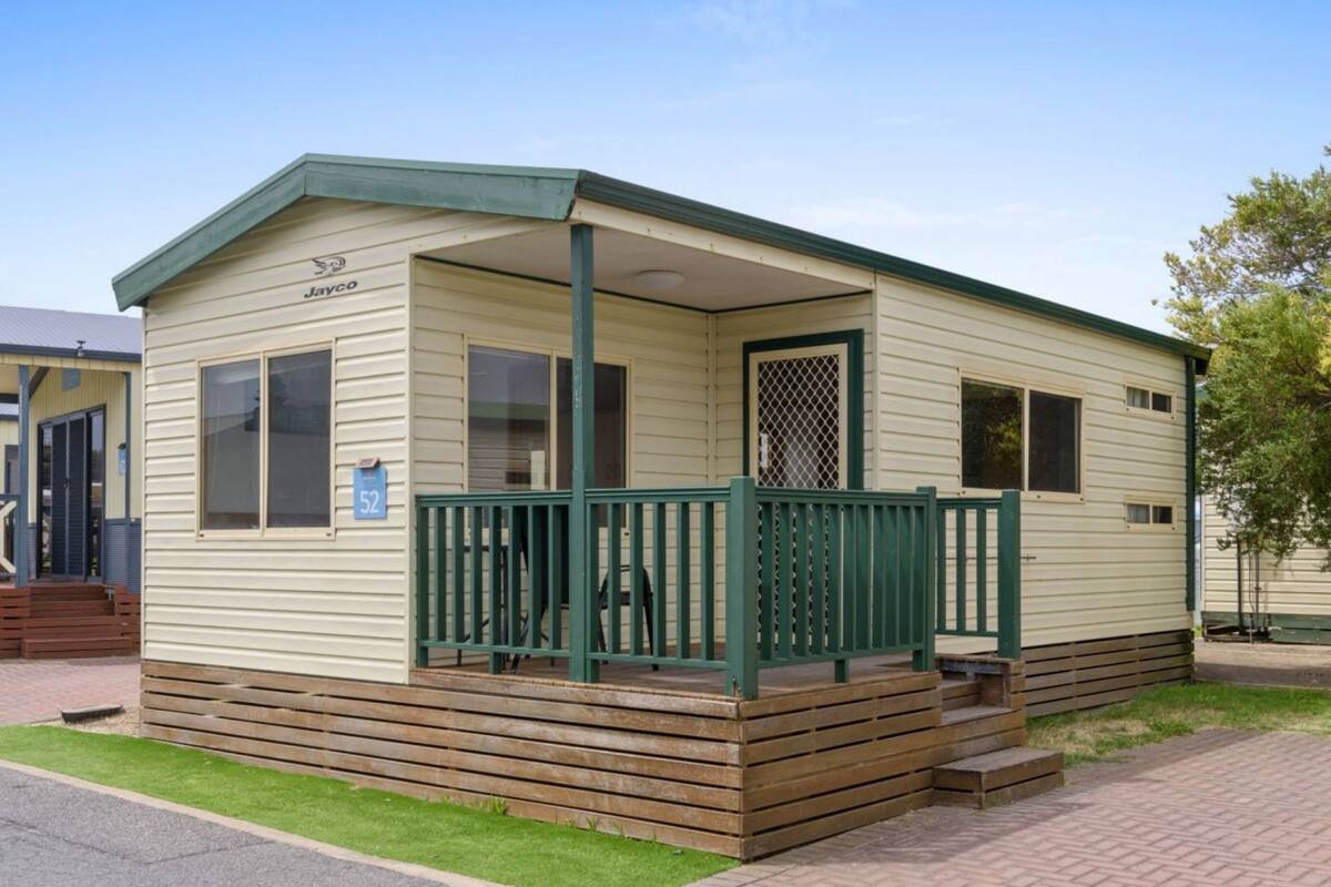 A small, single-story mobile home with a green porch and a number '52' sign.