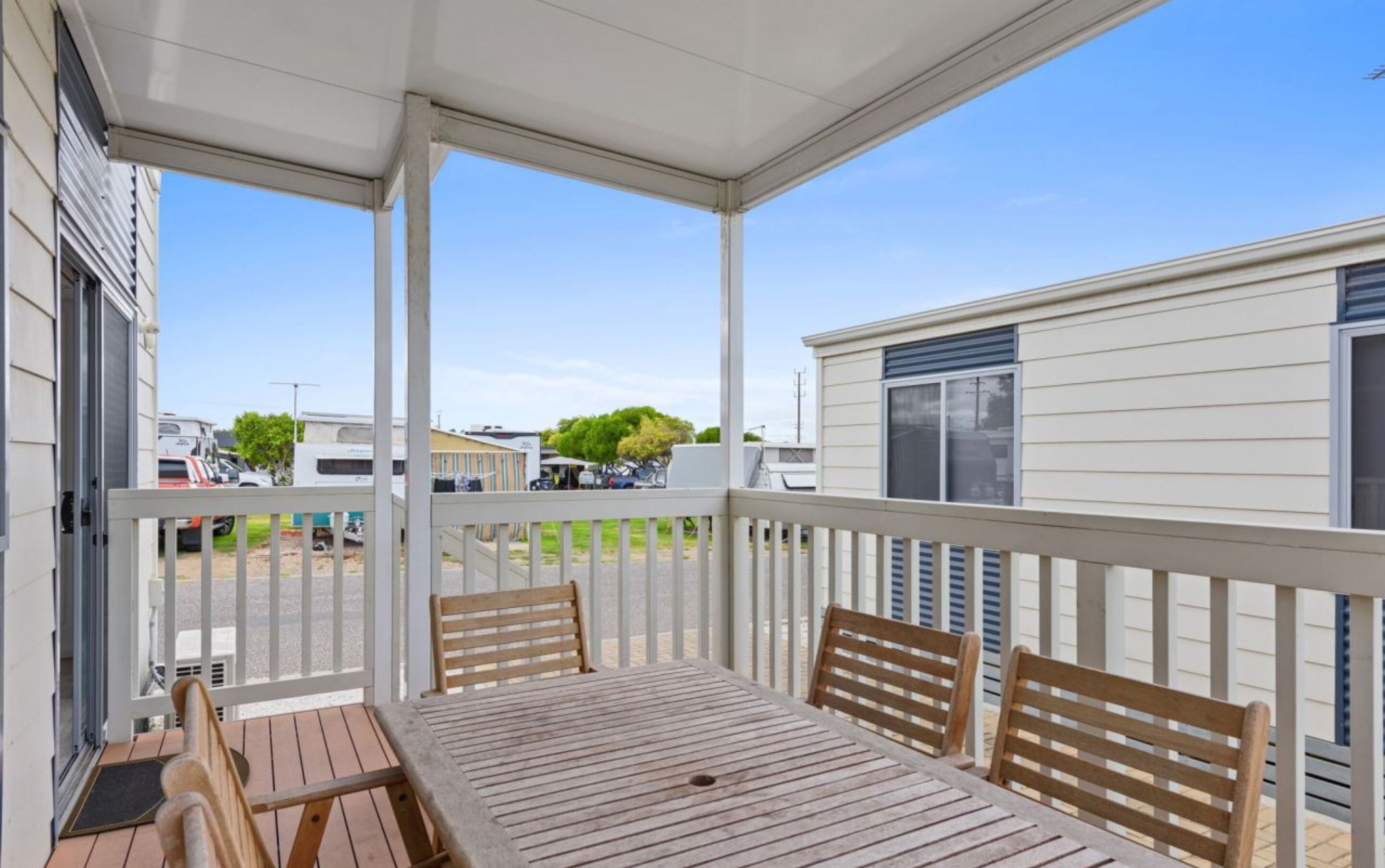 A covered patio with a table and chairs, overlooking a parking area with RVs and a building with a window.