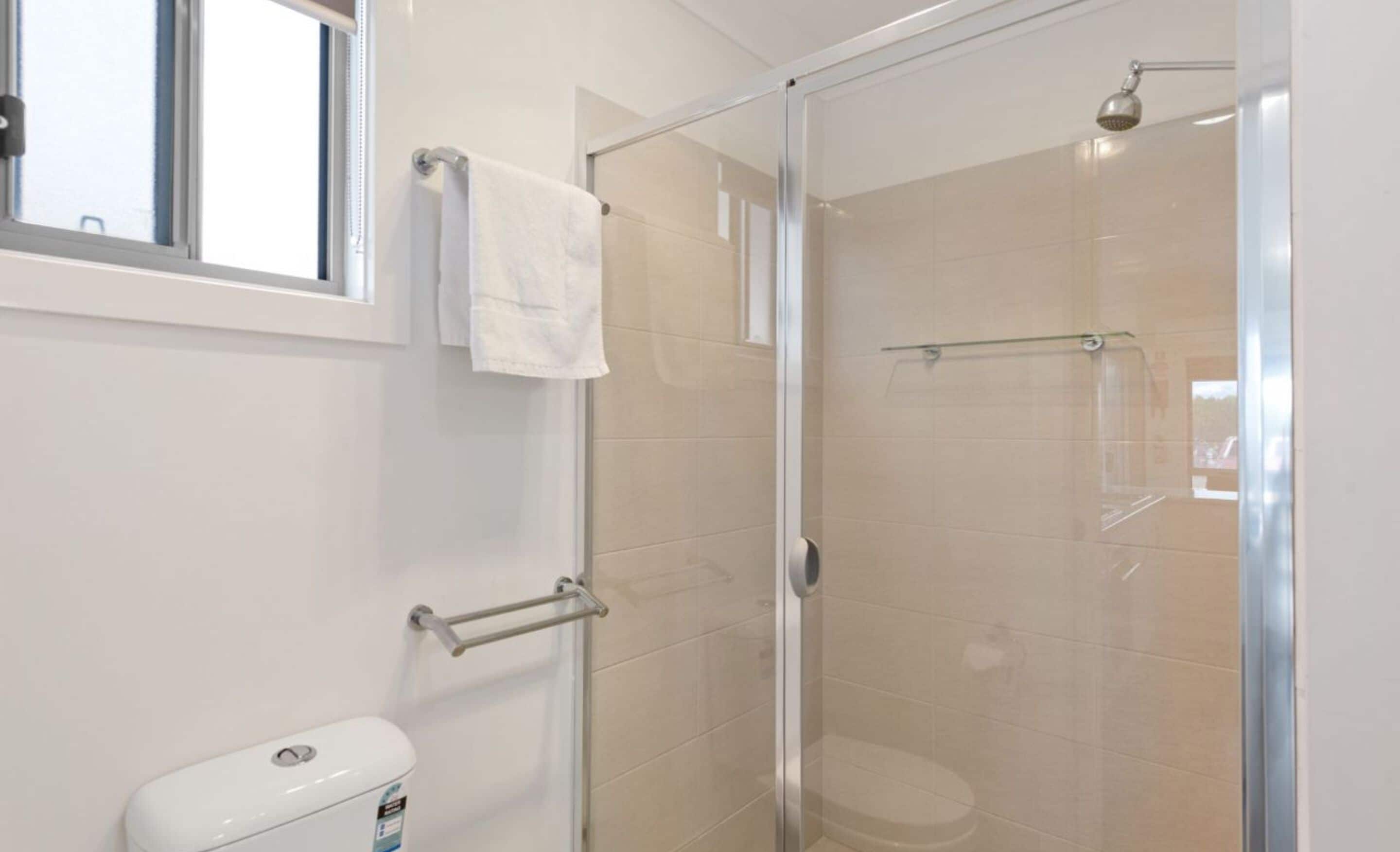A modern bathroom with a glass shower enclosure, a toilet, and a towel rack.