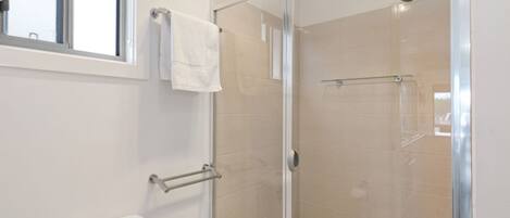 A modern bathroom with a glass shower enclosure, a toilet, and a towel rack.