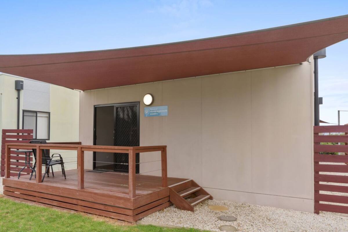 A covered outdoor area with a wooden deck, a table with chairs, and a sign indicating a room number.