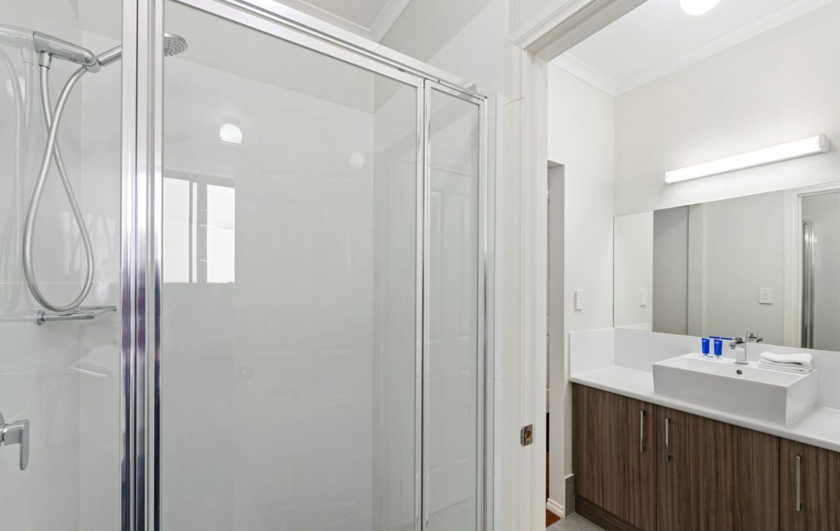 A modern bathroom with a glass shower enclosure, a white sink, and a large mirror.
