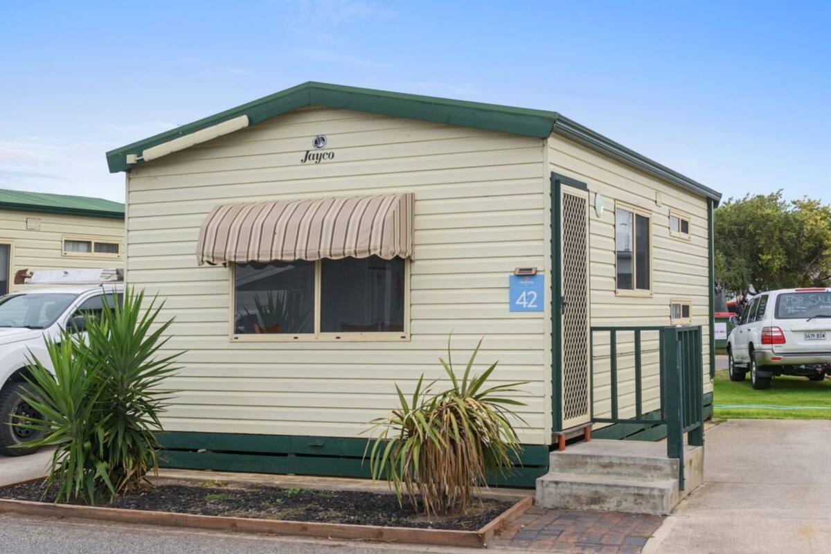A mobile home with a green roof, beige siding, and a number 42 sign.