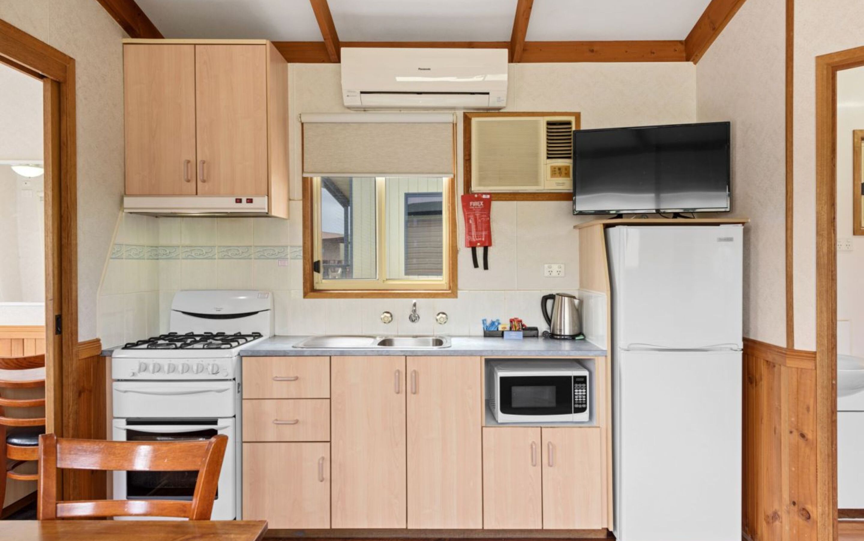 A compact kitchen with wooden cabinets, a gas stove, a microwave, a refrigerator, and a television.