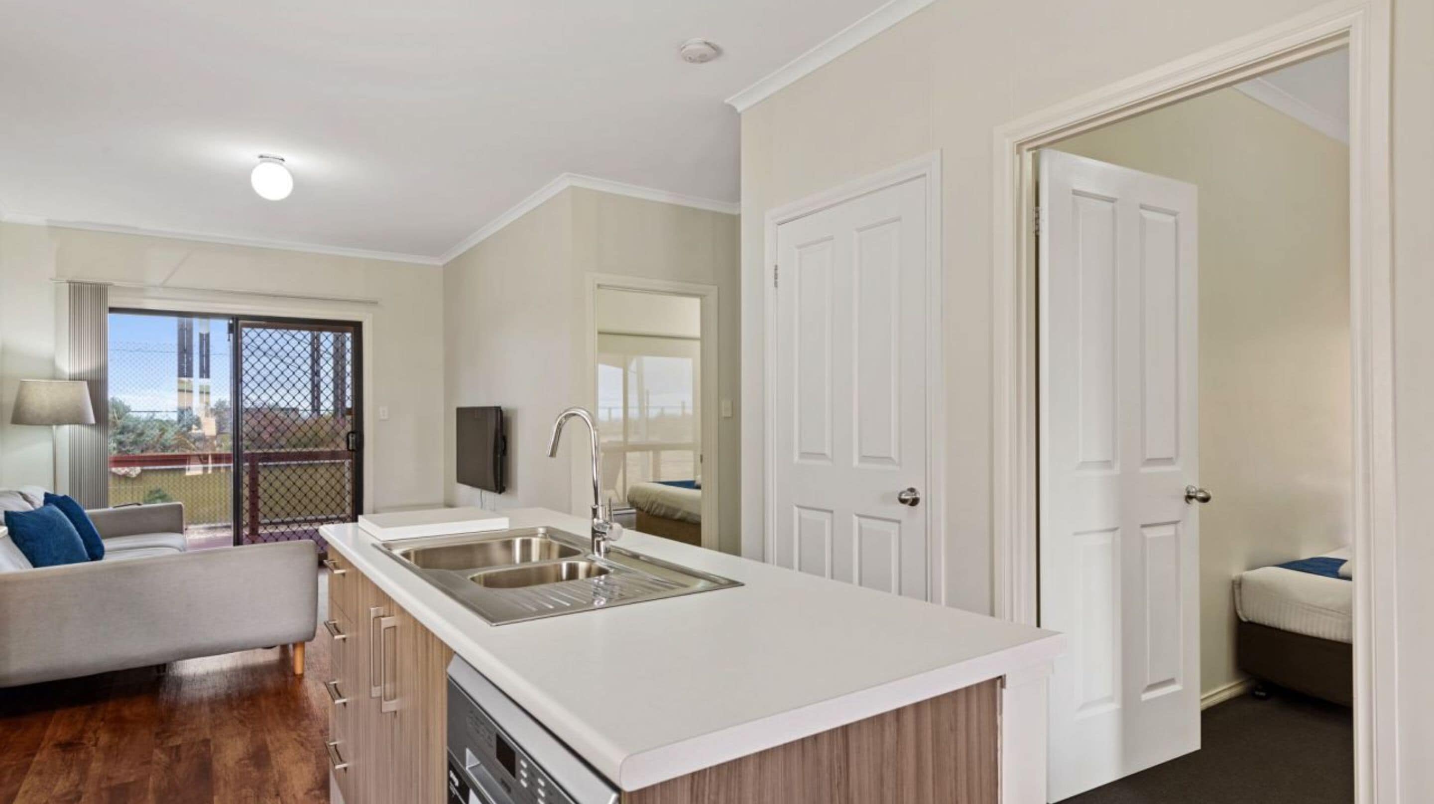 A modern kitchen with a central island, white cabinetry, and a large window overlooking a balcony.
