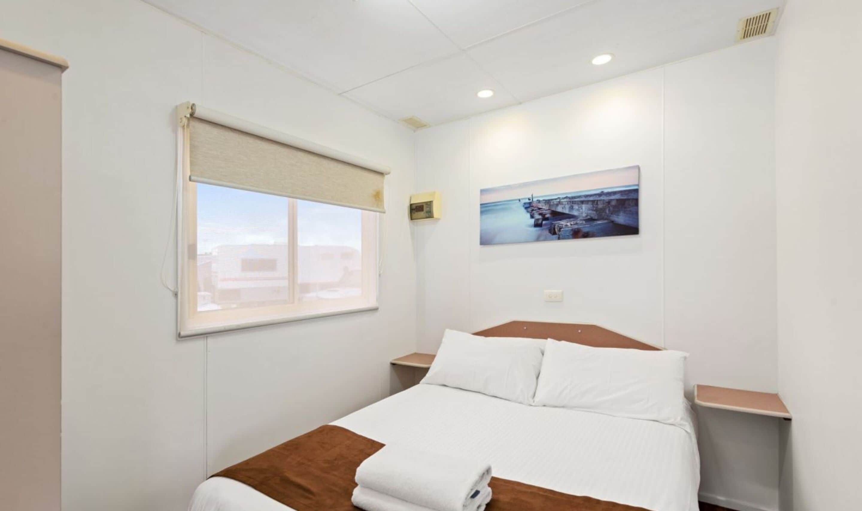 Ein Hotelzimmer mit Bett, Fenster mit Blick, einem Bild an der Wand und einem Thermostat.