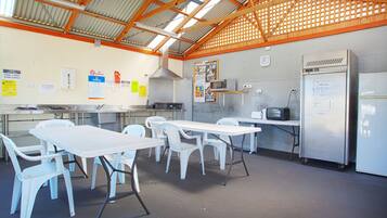 A spacious indoor area with tables and chairs, a kitchen area with appliances, and a clock on the wall.