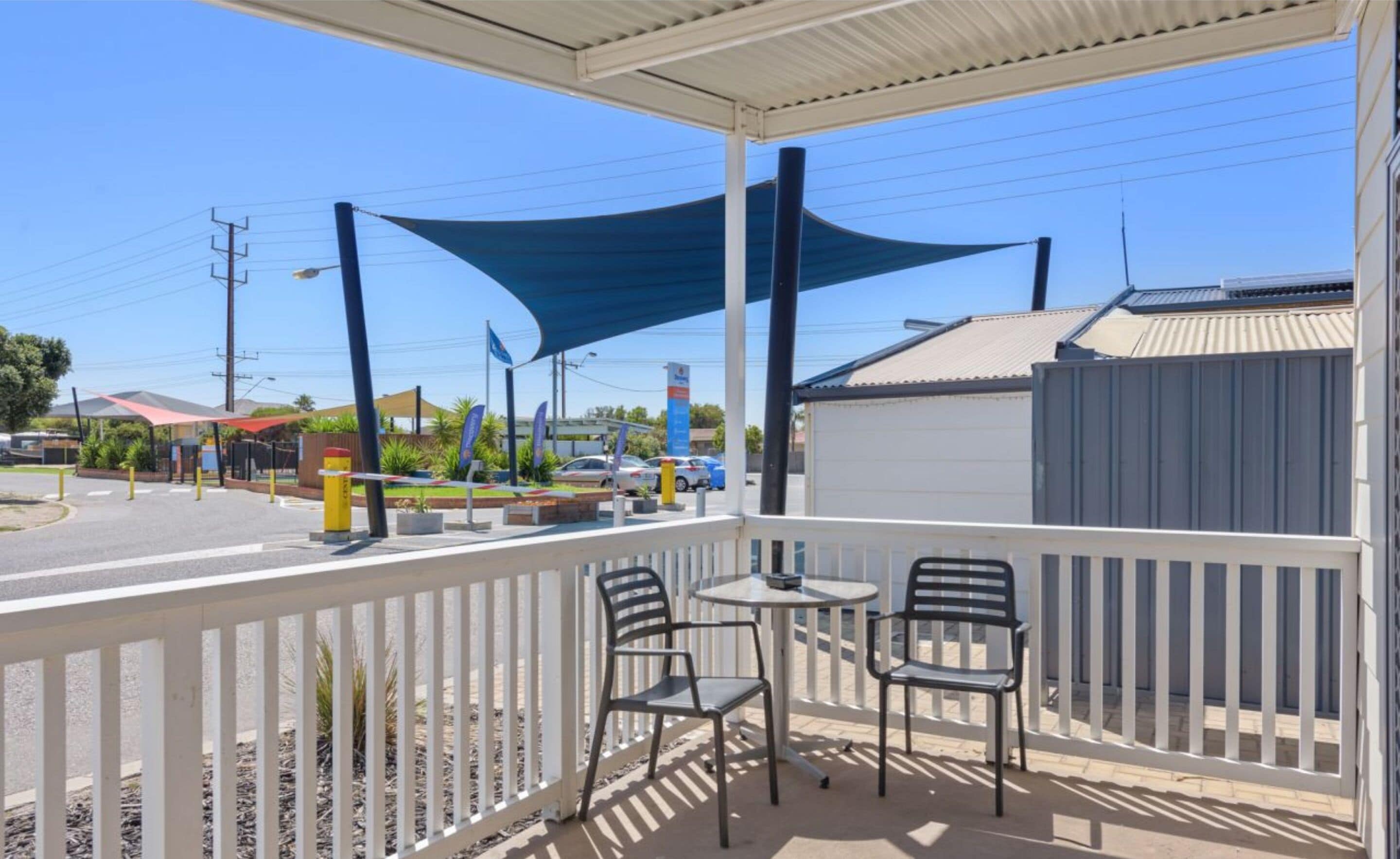 A covered outdoor seating area with two chairs and a table, overlooking a street with cars and buildings.