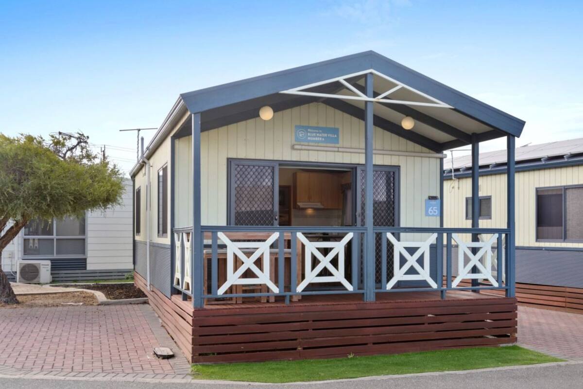 A small, single-story structure with a covered porch and a sign indicating it is a Blue Water Villa numbered 65.