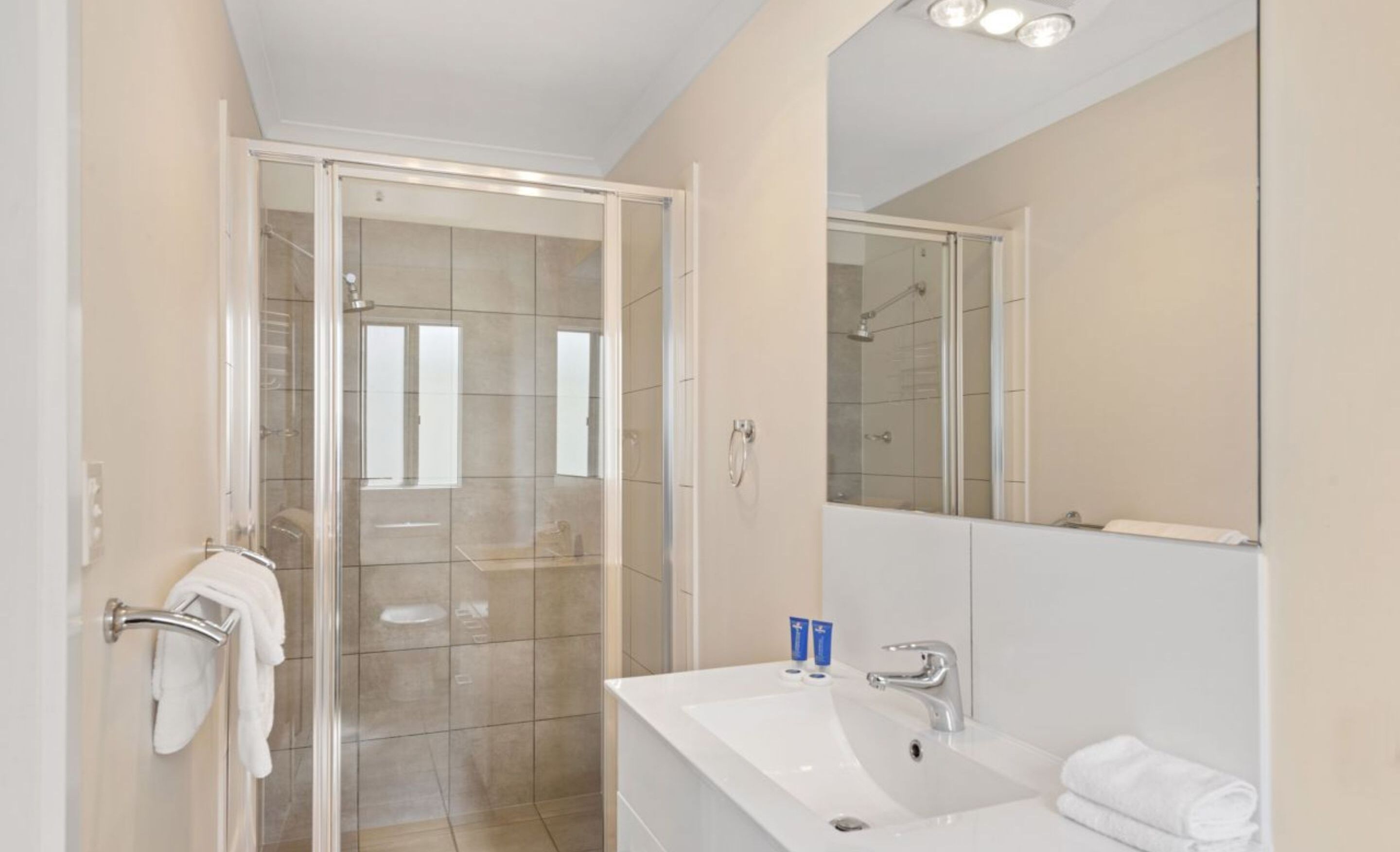 A modern bathroom with a glass shower enclosure, a white sink with a mirror, and a towel rack.