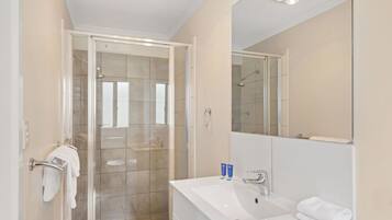 A modern bathroom with a glass shower enclosure, a white sink with a mirror, and a towel rack.