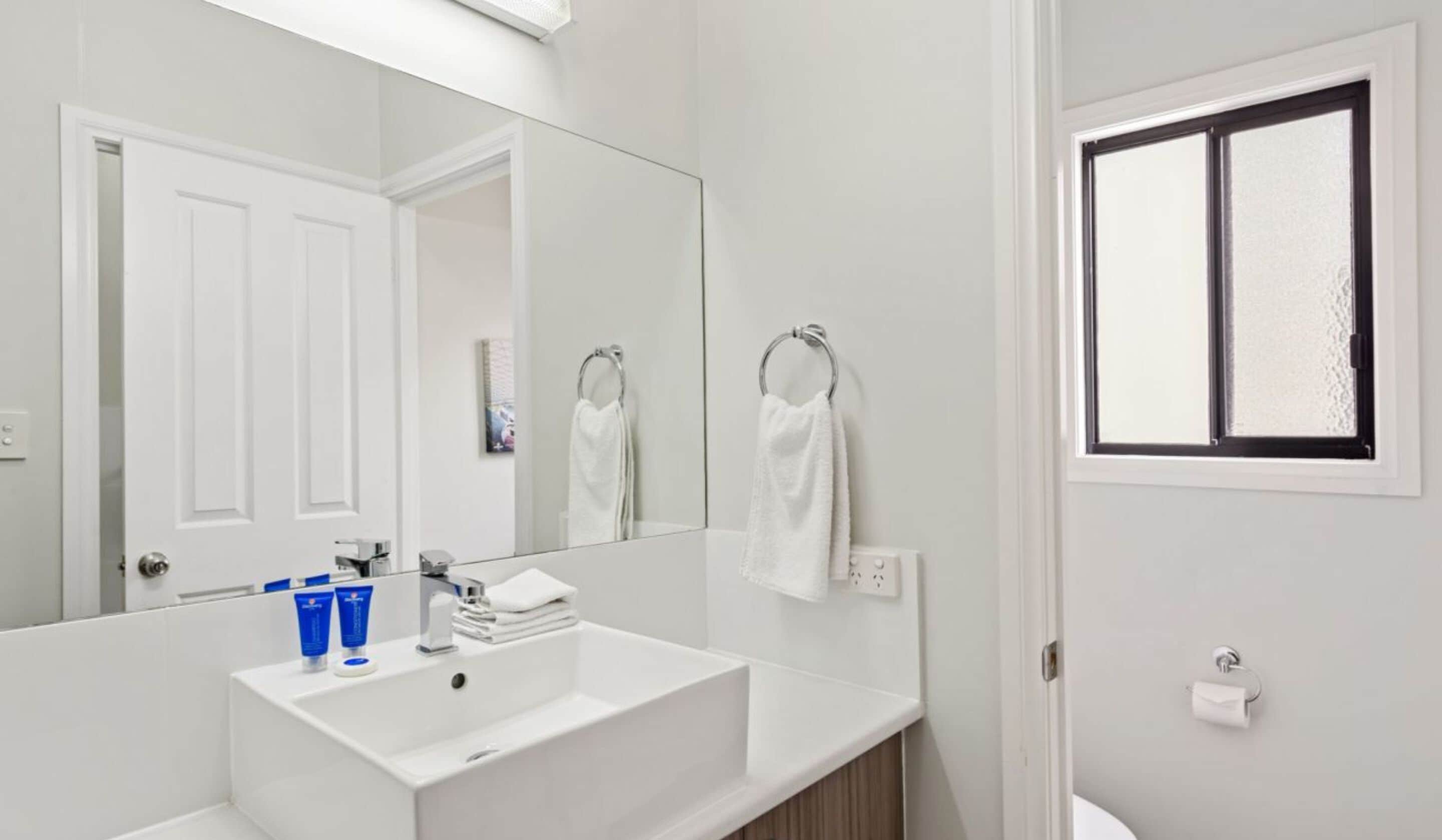 Une salle de bain moderne avec un lavabo blanc, un grand miroir et une fenêtre en verre dépoli.