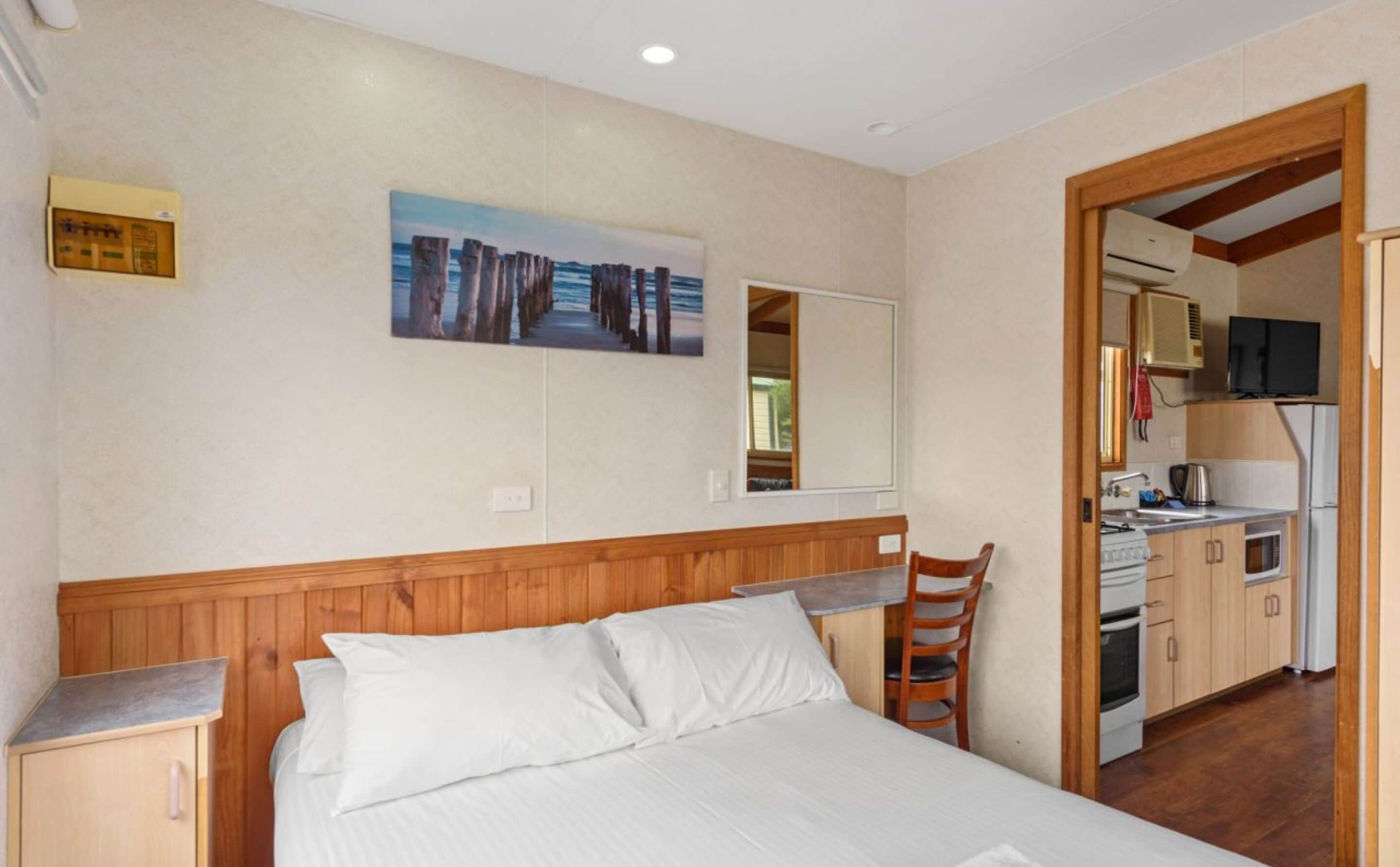 A bedroom with a bed, a wooden headboard, a desk, and a painting on the wall.